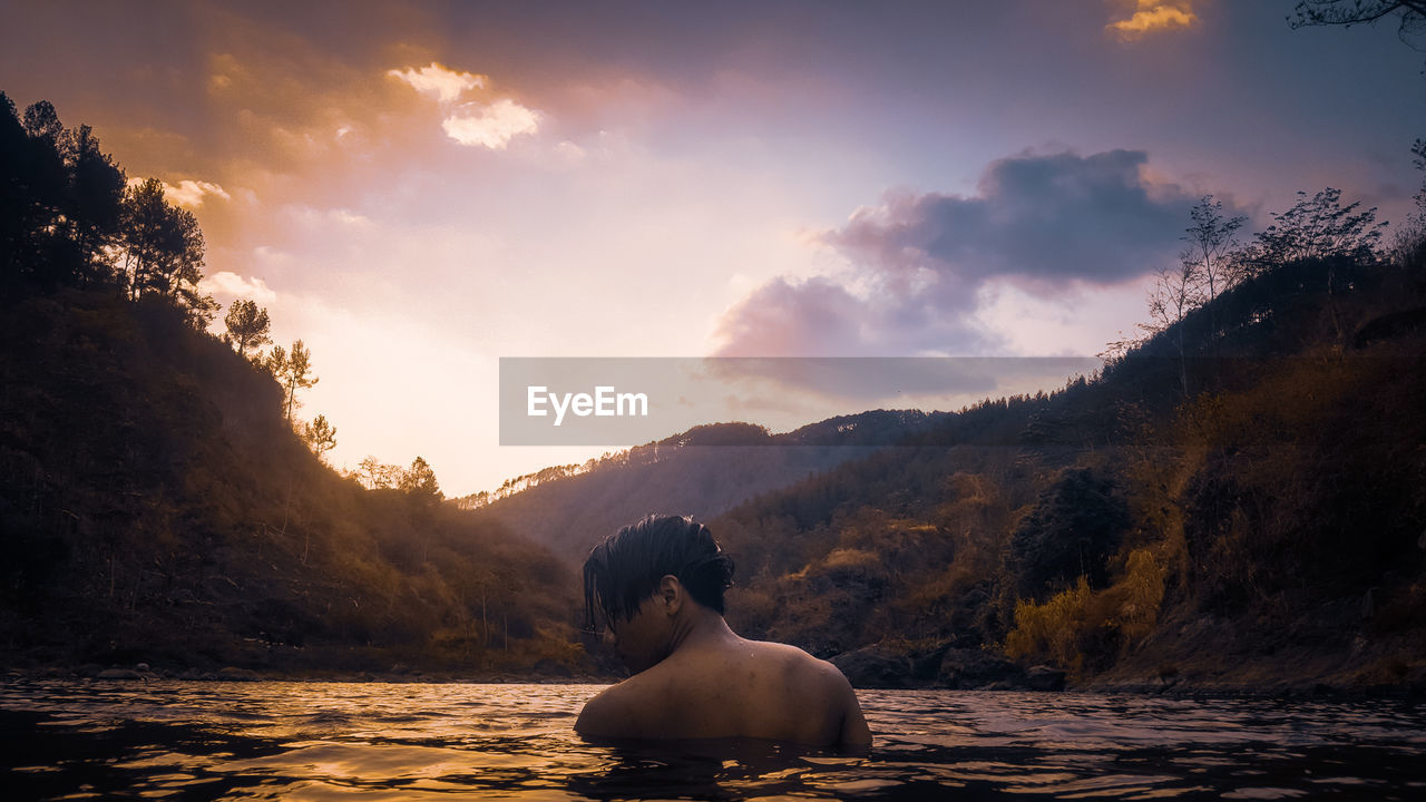 MAN SITTING BY MOUNTAIN AGAINST SKY