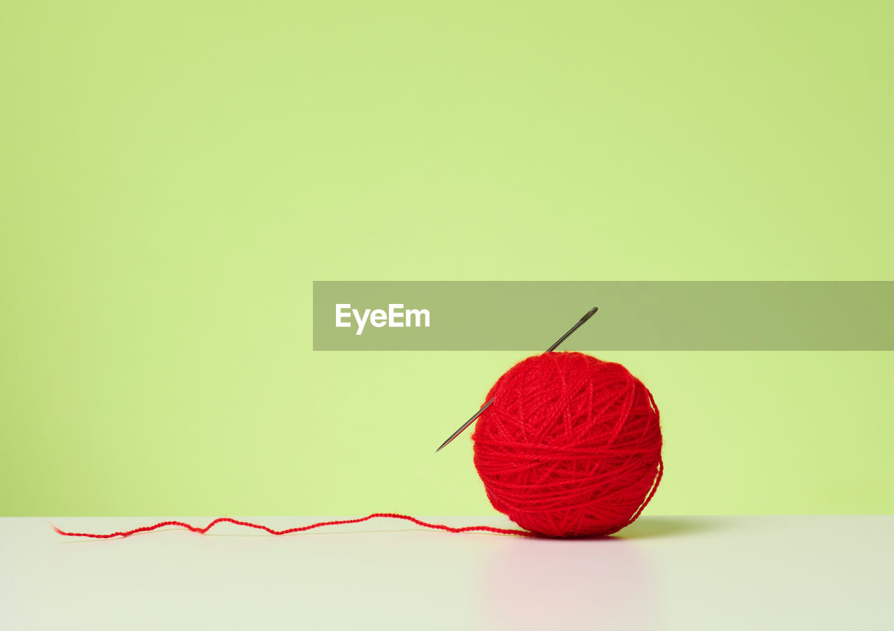 Red ball with woolen thread on white table, green background