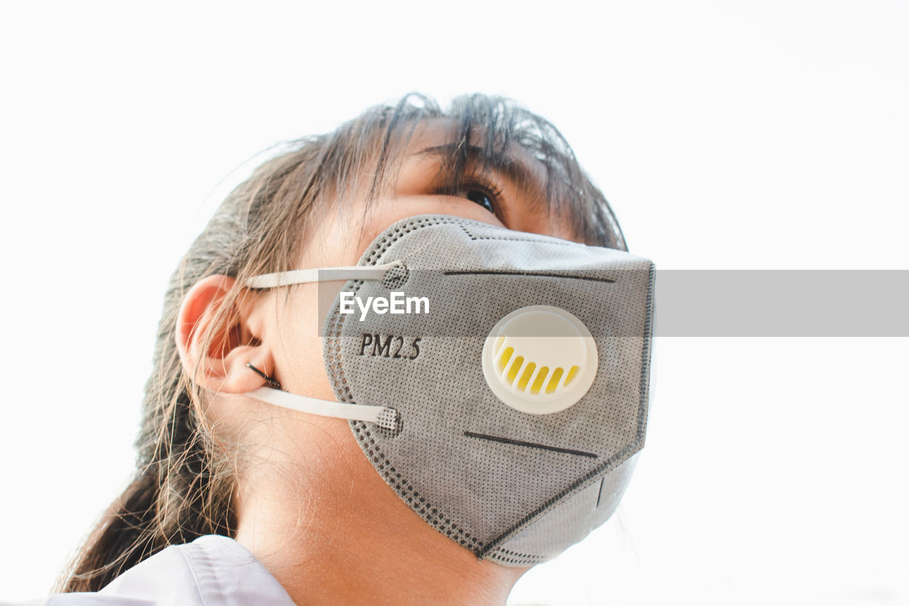 Close-up of girl wearing pollution mask against sky