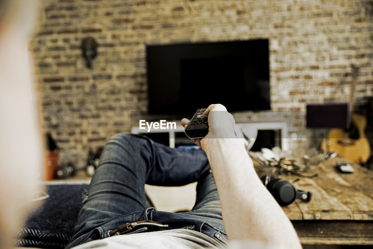 Man lying on the couch using remote control, partial view