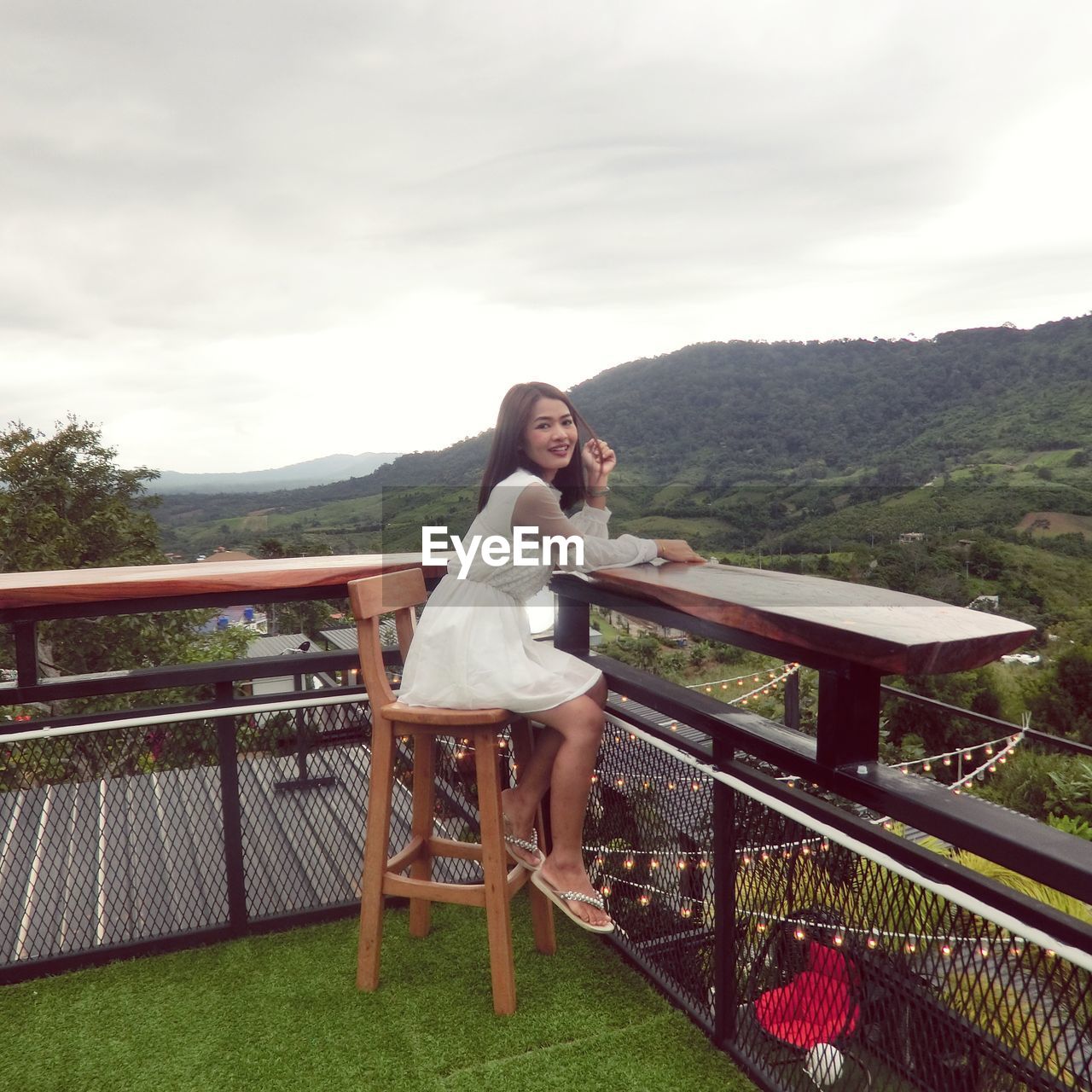 FULL LENGTH OF YOUNG WOMAN ON RAILING AGAINST SKY