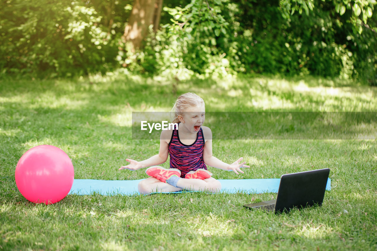 Angry mad girl child doing sport workout outdoors online. video yoga class on internet. 