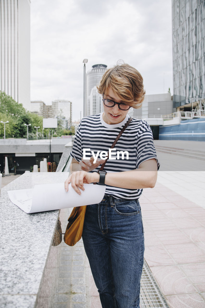 Businesswoman using smart watch standing near wall in city