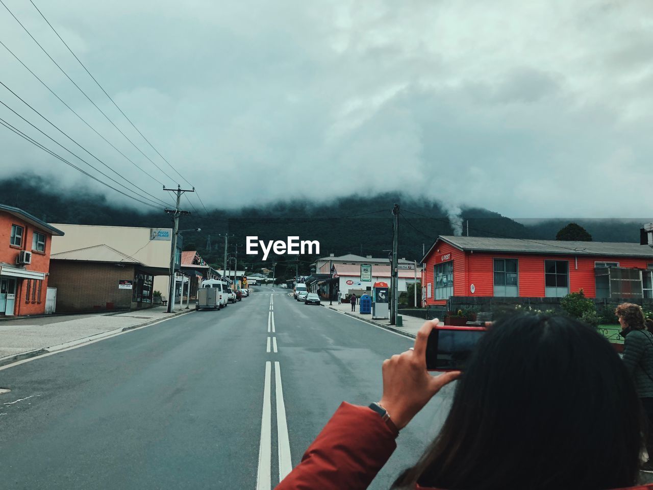 Woman photographing cloudy sky in city