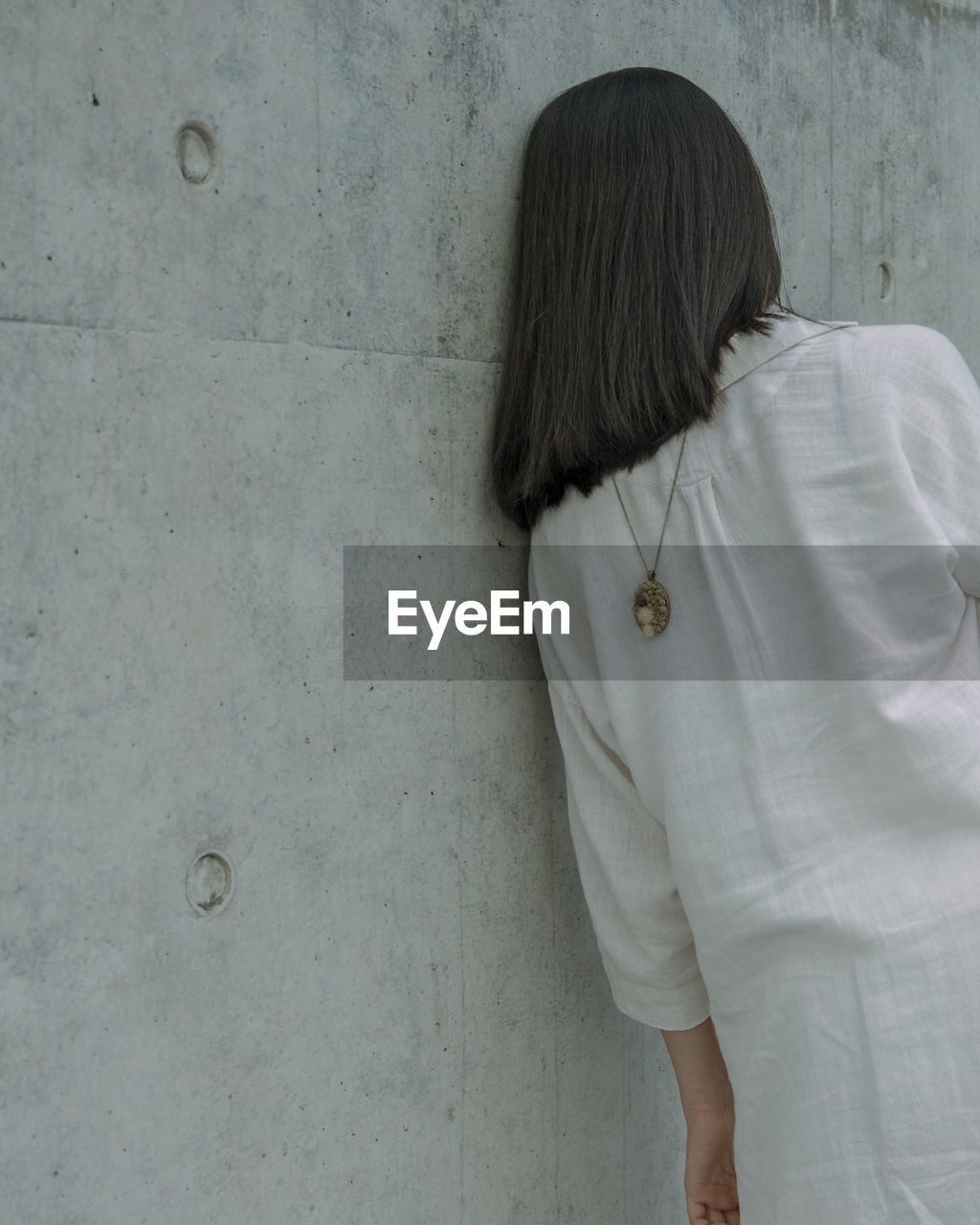 Rear view of young woman wearing chain while leaning on wall