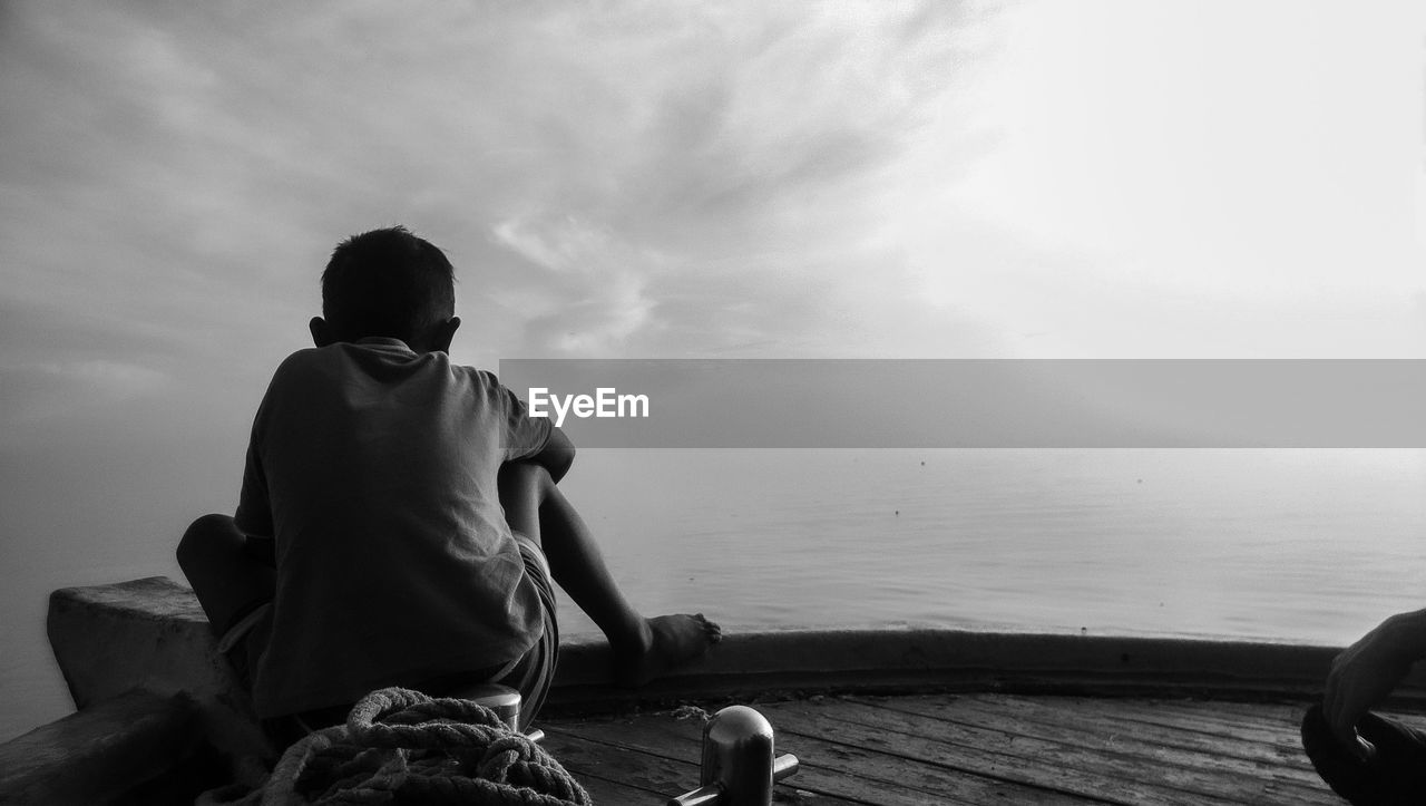 Rear view of man sitting by sea against sky