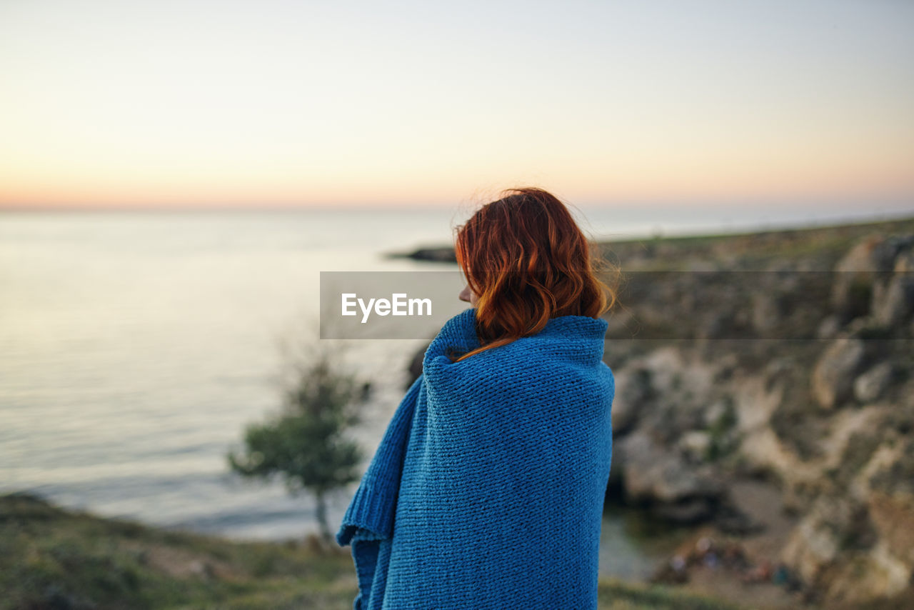 REAR VIEW OF WOMAN LOOKING AT SEA DURING SUNSET