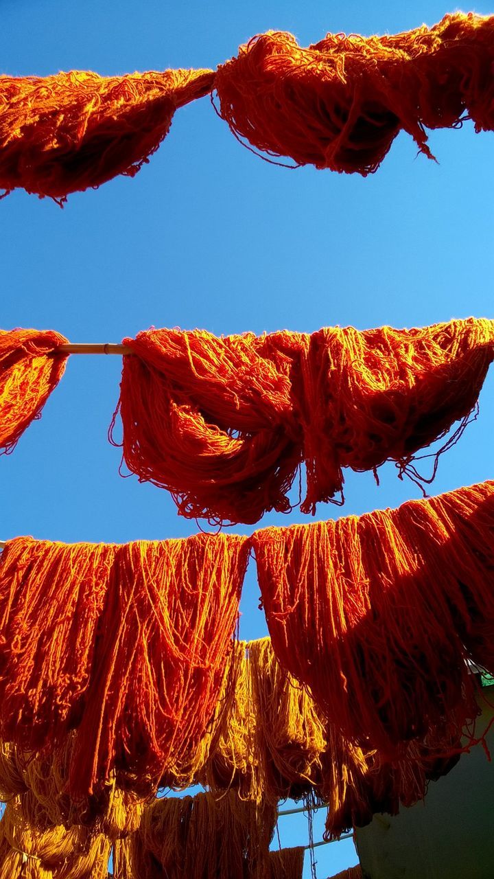 Low angle view of orange fishing nets hanging against sky