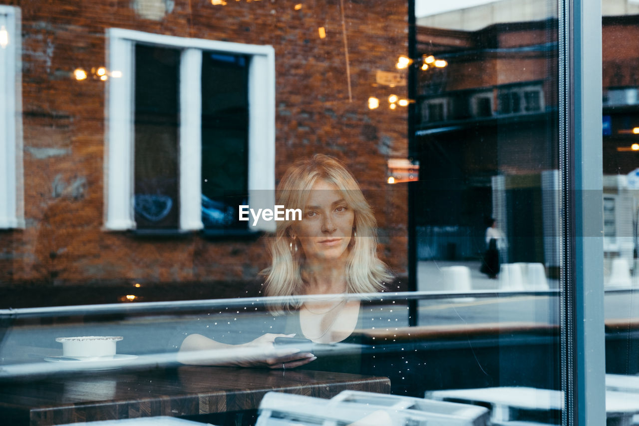 PORTRAIT OF WOMAN LOOKING THROUGH WINDOW AT GLASS