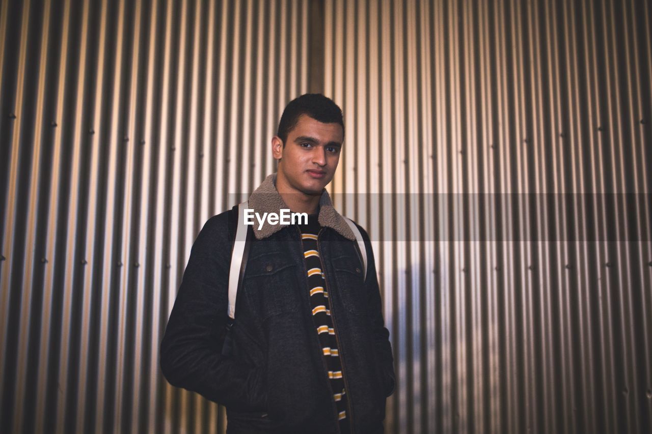 Portrait of young man with hands in pockets standing against wall