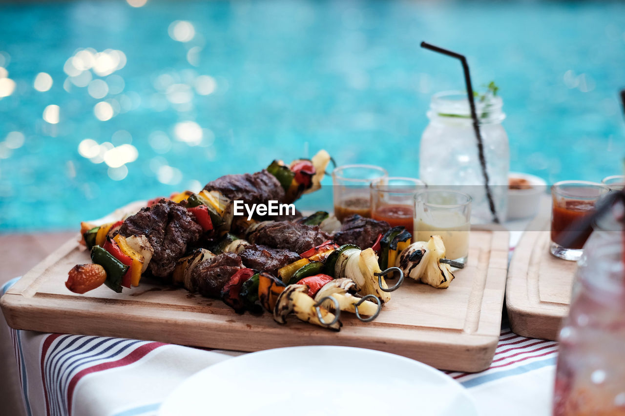 High angle view of barbecued meat and vegetables in skewers on tray at pool party