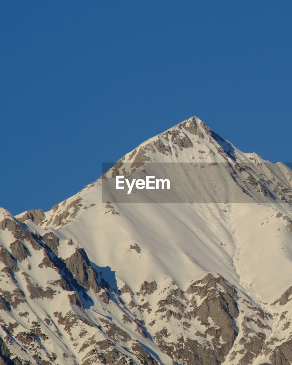 Low angle view of snowcapped mountains against clear blue sky