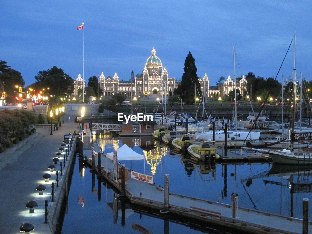 Illuminated parliament building by boats moored on lake at dusk