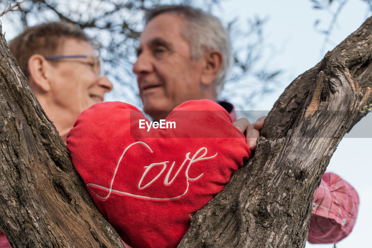 A happy old man and a woman with a red heart and the word love each other on the trunk