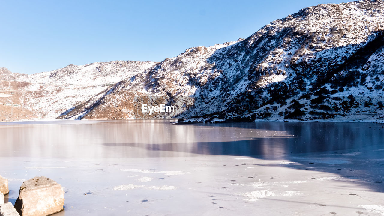 FROZEN LAKE BY SNOWCAPPED MOUNTAINS AGAINST SKY