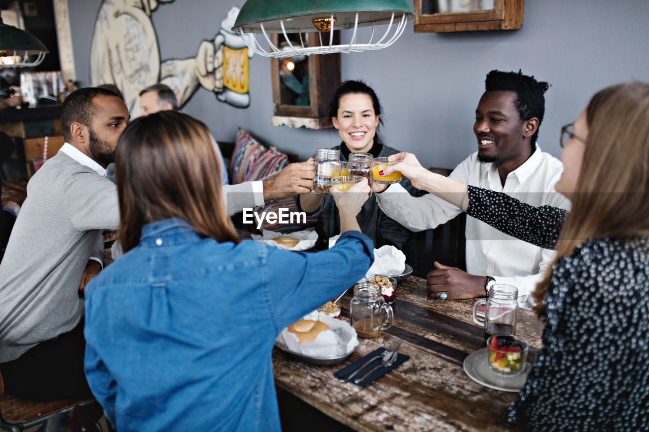 Happy friends toasting drink while sitting at dining table in restaurant