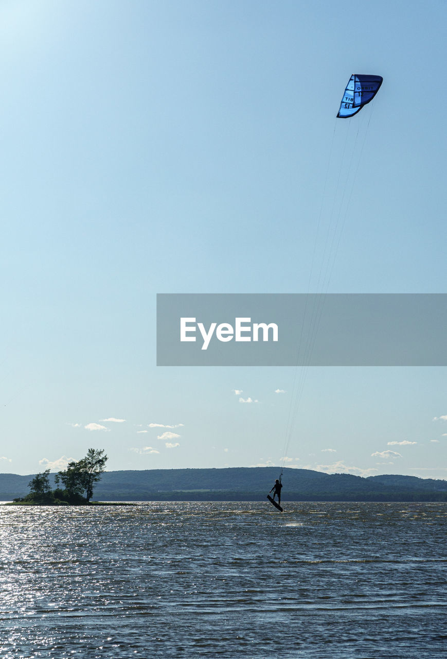 Person paragliding over sea against sky