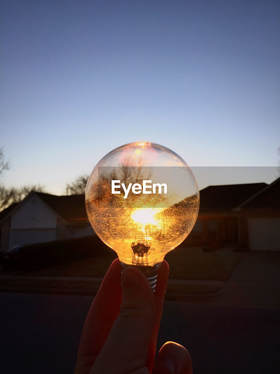 Optical illusion of hand holding bulb against sun during sunset