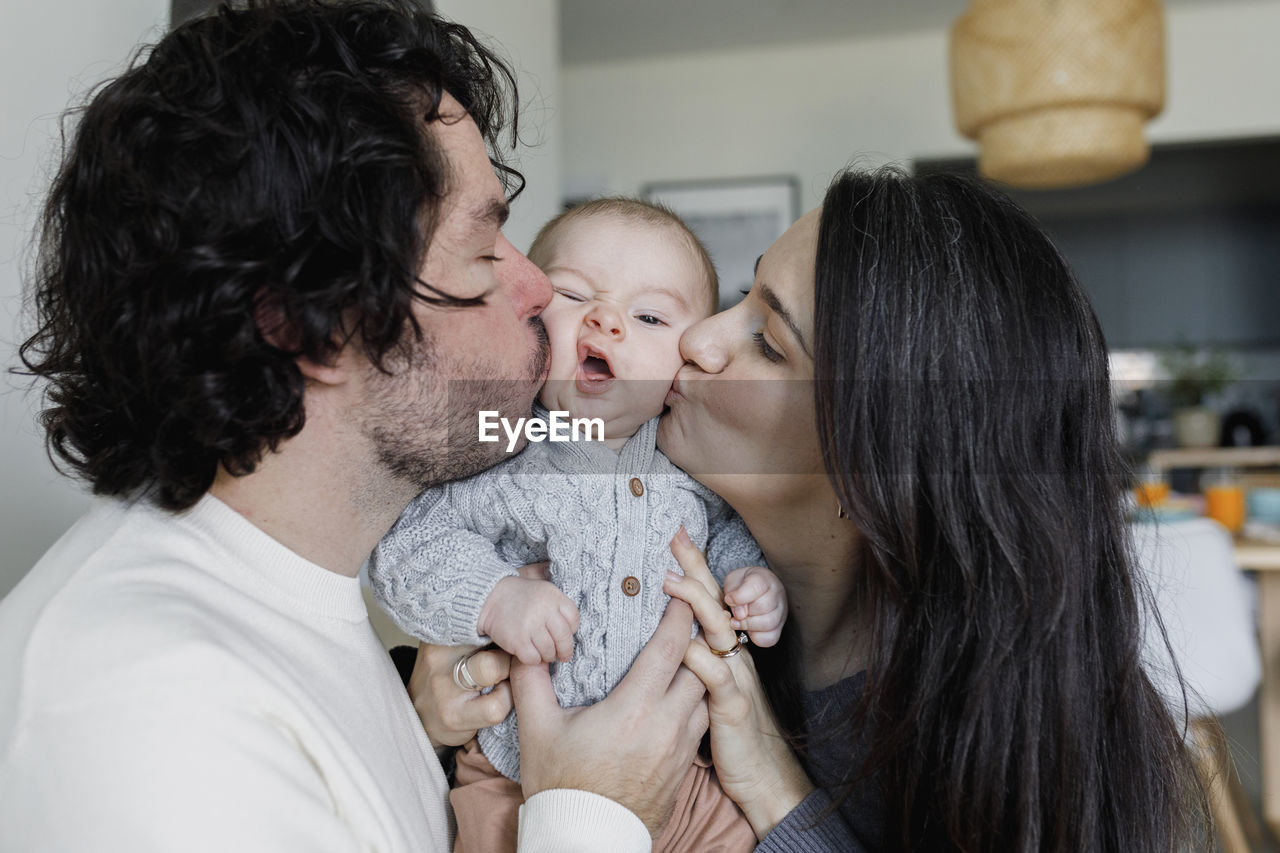 Father and mother kissing baby boy at home