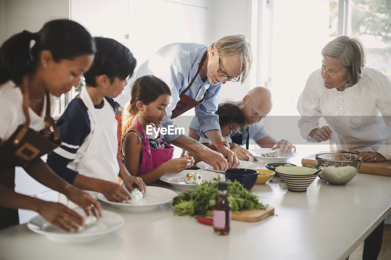 Senior woman guiding family in preparing asian food in kitchen