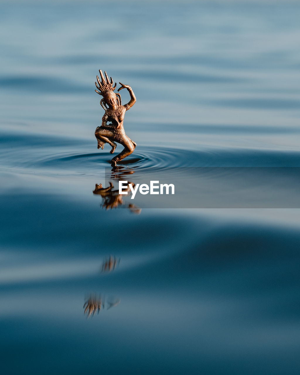 Bronze statuette of hindu goddess dancing on waves of clean blue water in nature