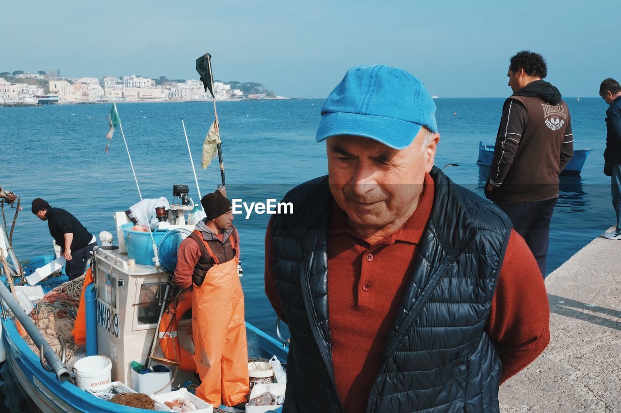 PANORAMIC SHOT OF PEOPLE STANDING ON SEA SHORE AGAINST CLEAR SKY