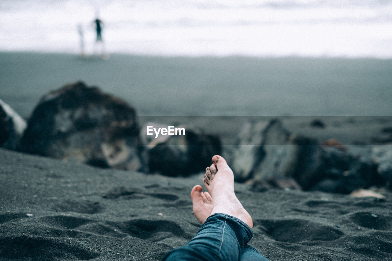 Low section of person sitting on sand at beach