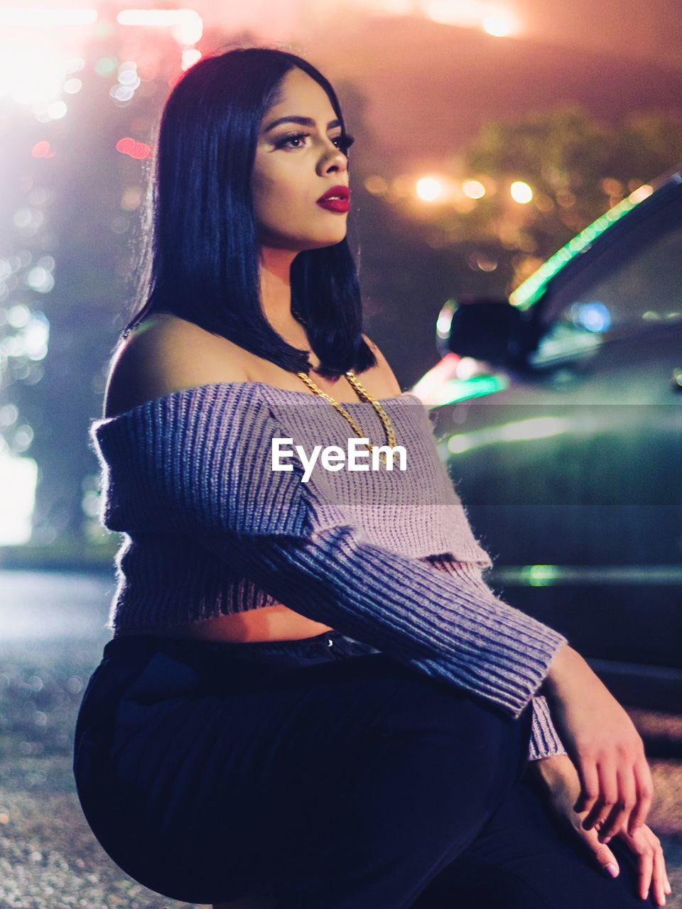 Young woman crouching by car on road at night