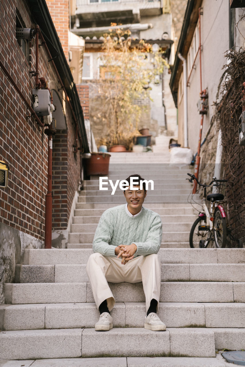 PORTRAIT OF A SMILING YOUNG MAN SITTING ON STAIRCASE