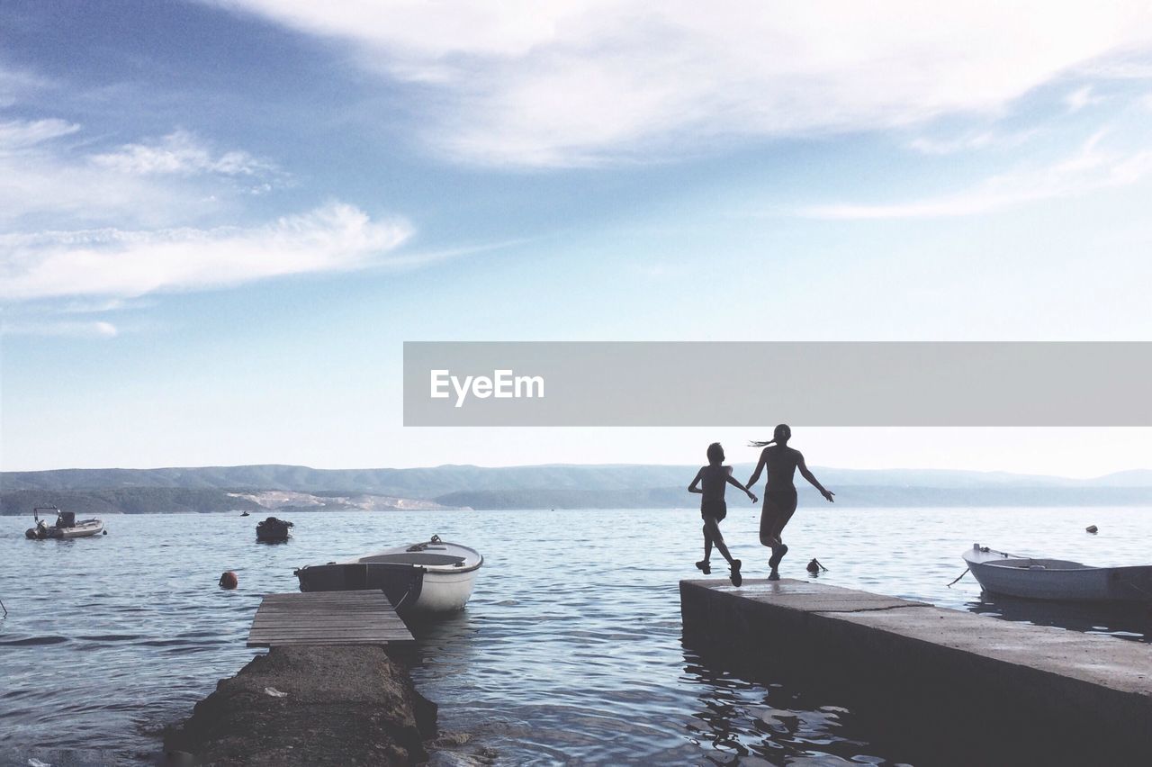 Rear view of siblings on pier against sea