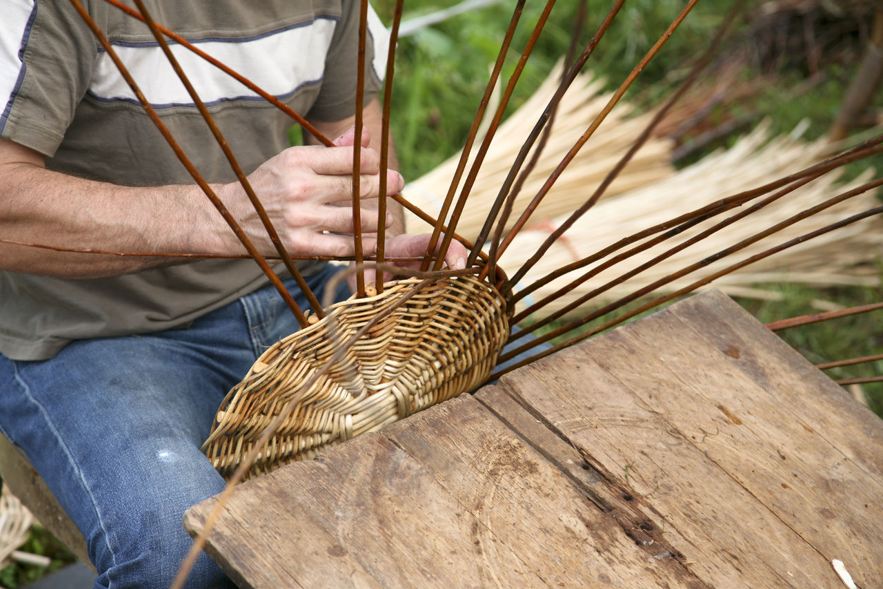 Midsection of man making wicker basket while sitting outdoors