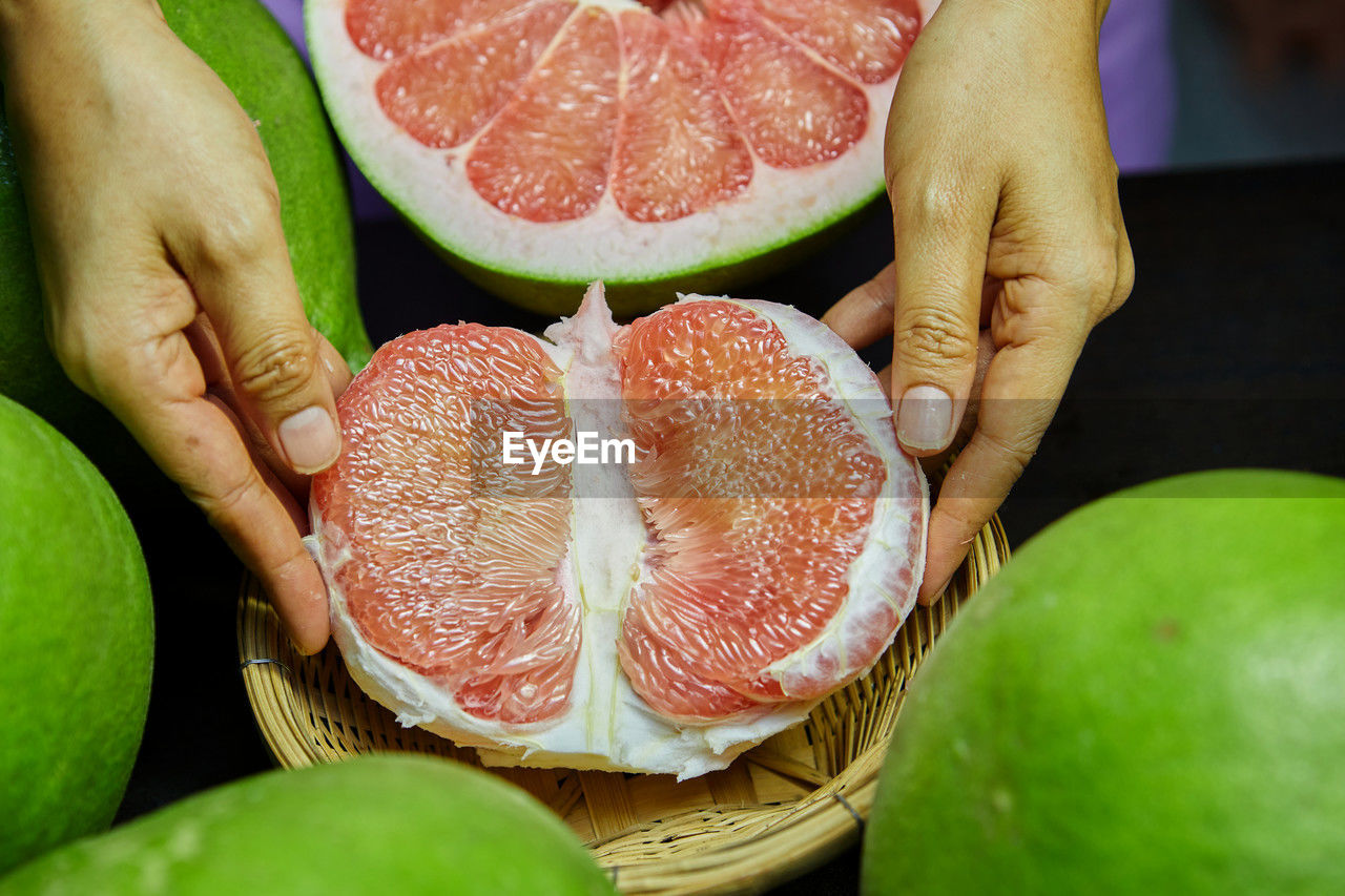Cropped hand holding ripe siam ruby pomelo fruit on table