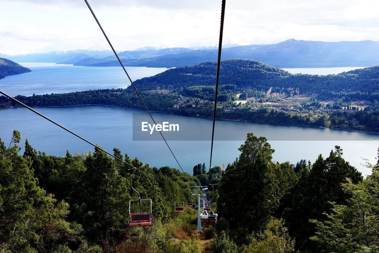 High angle view of ski lifts over forest and river against sky