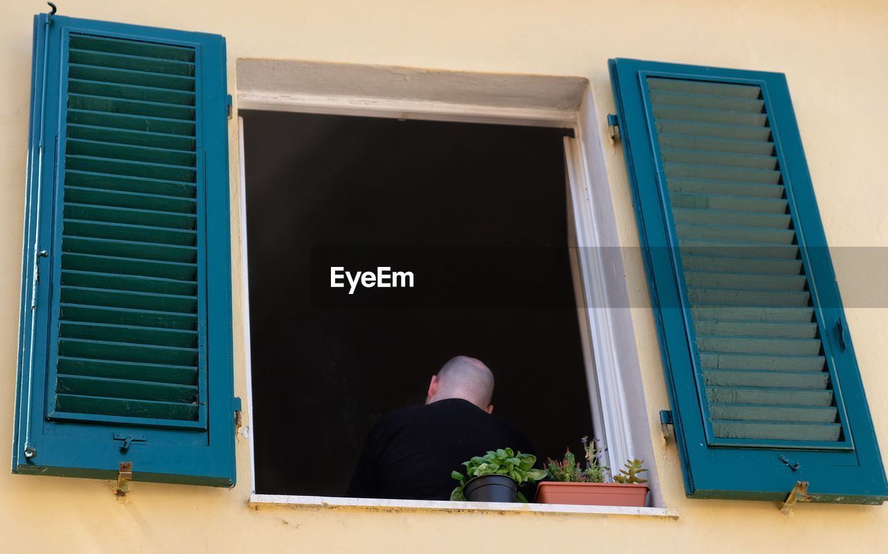 REAR VIEW OF MAN STANDING AGAINST WINDOW