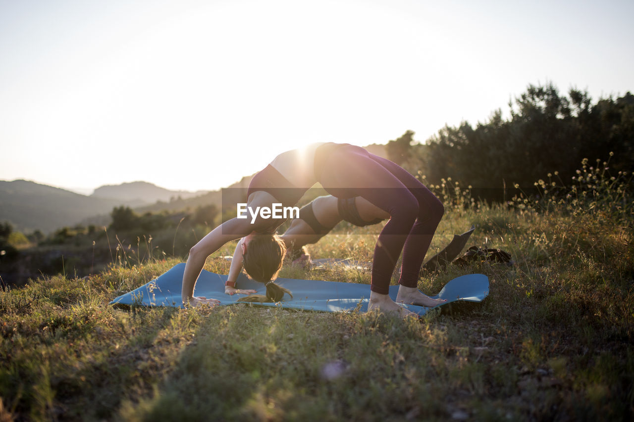 Side view of woman exercising on filed against sky