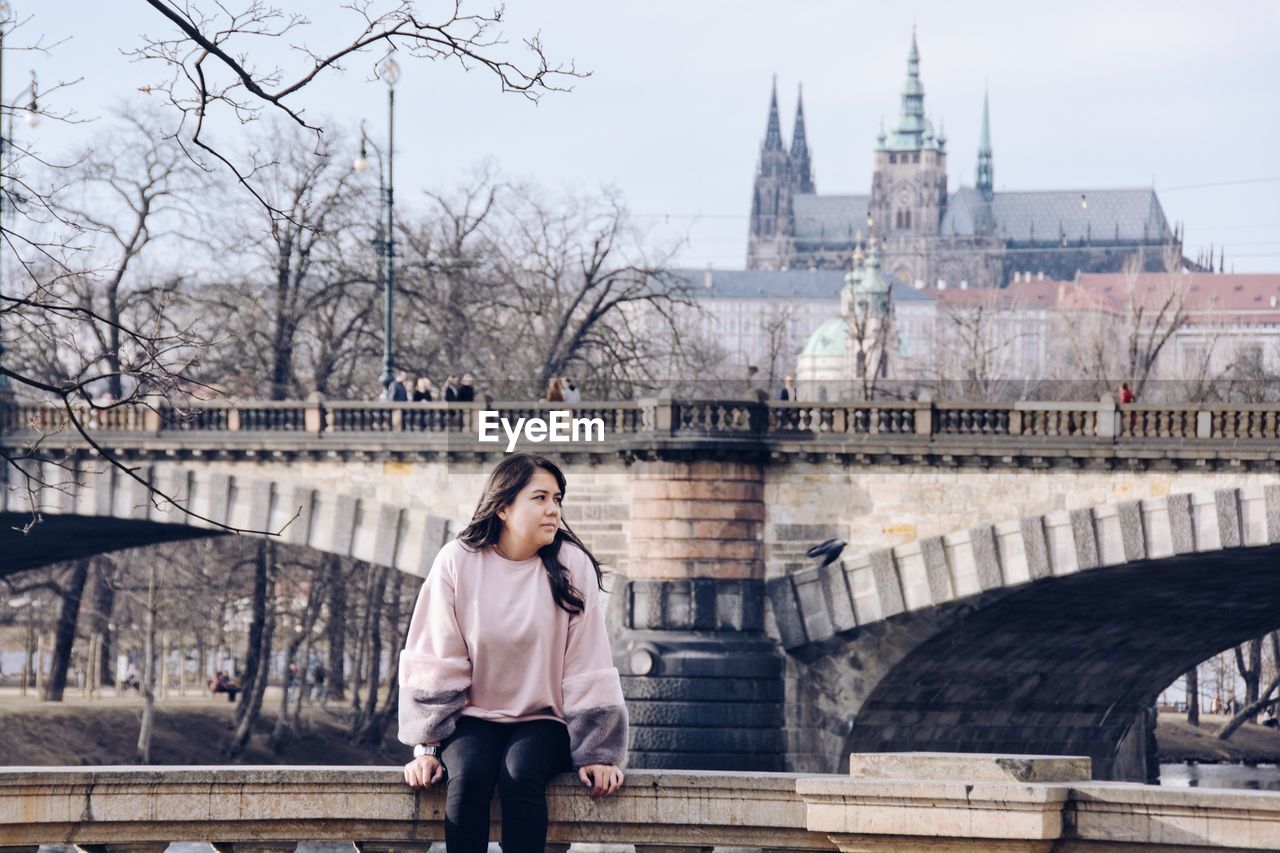 Young woman sitting against bridge in city