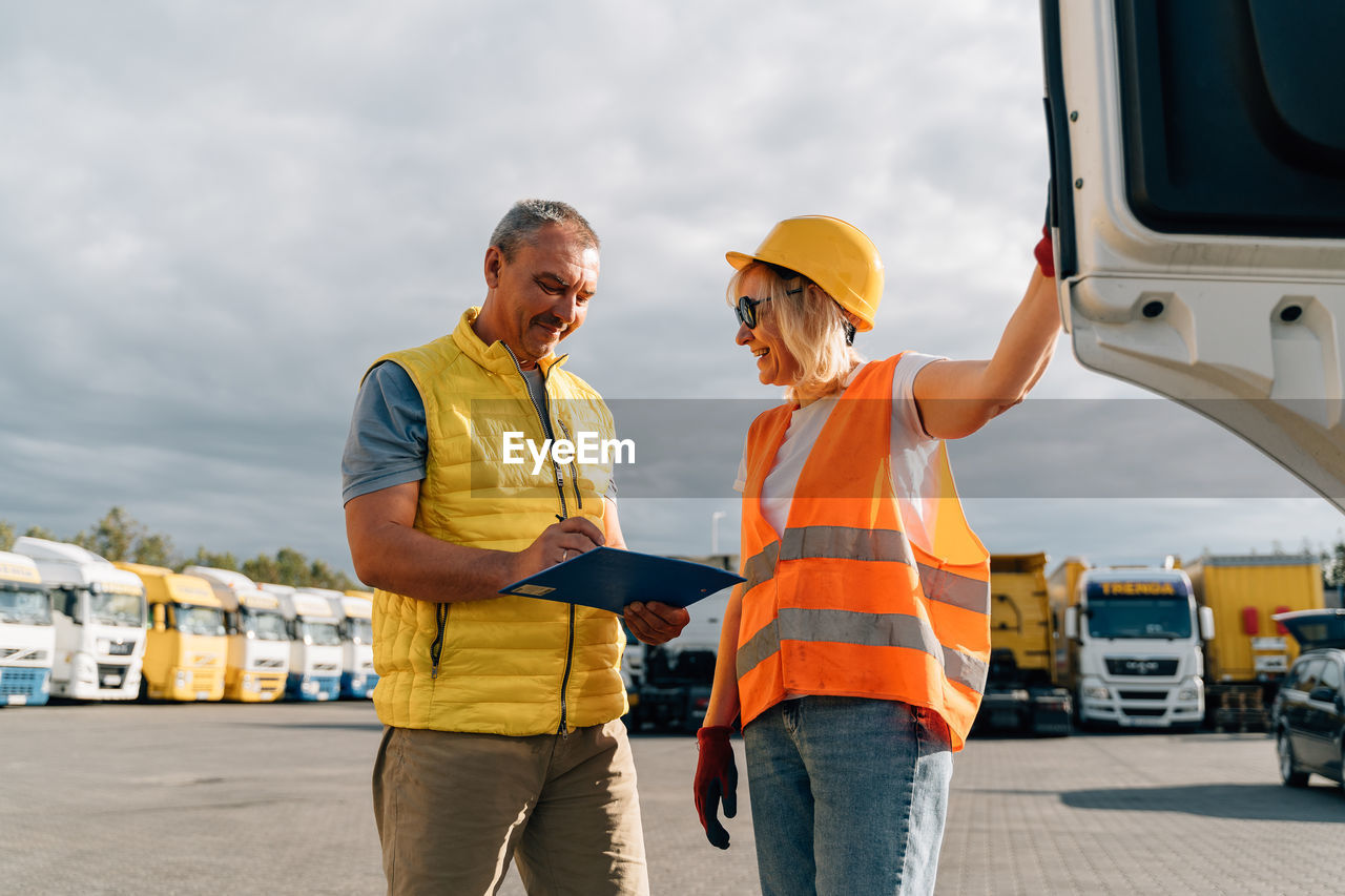 Smiling man writing on file folder standing by woman