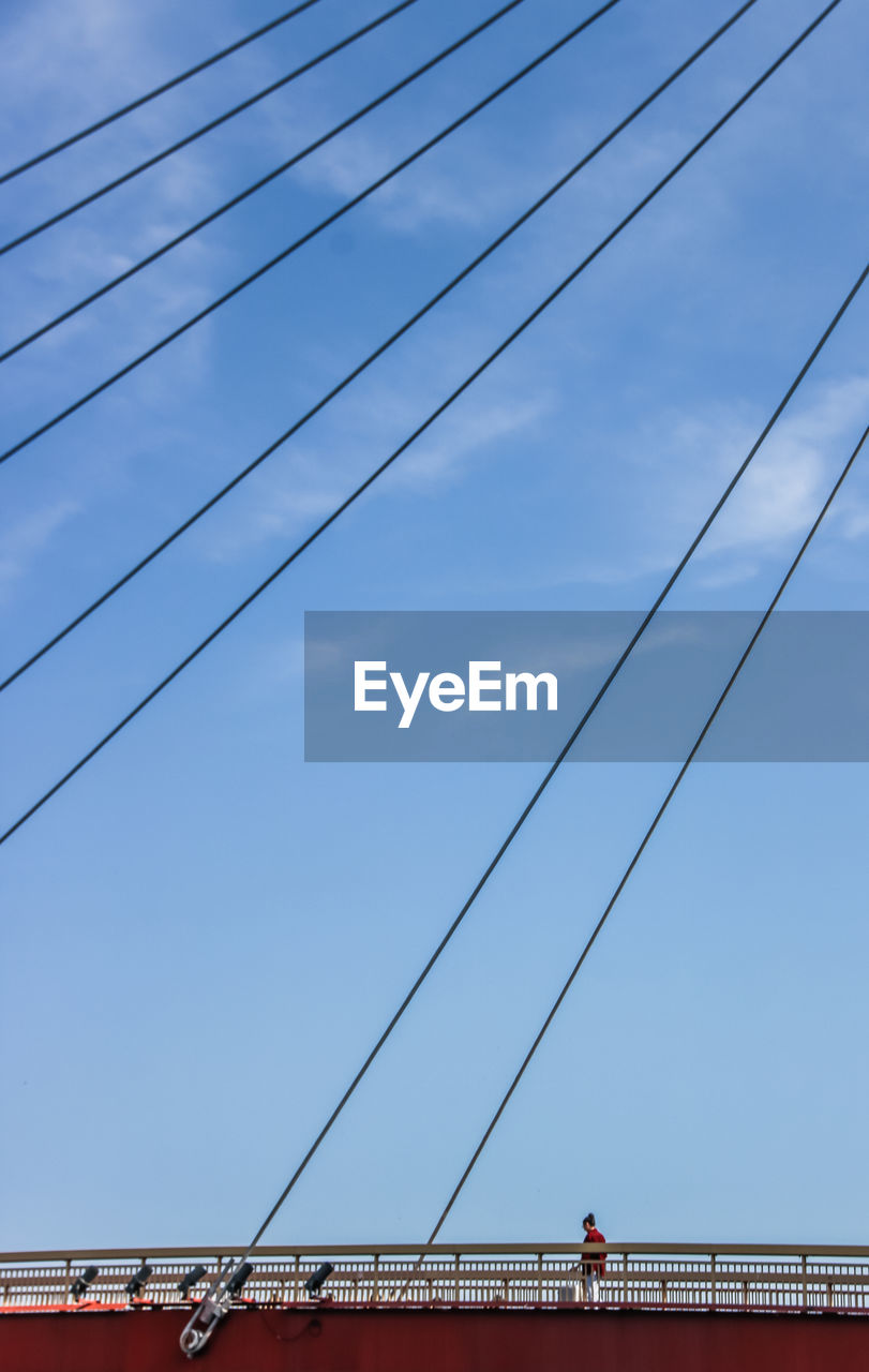 Distant view of man walking on bridge against blue sky