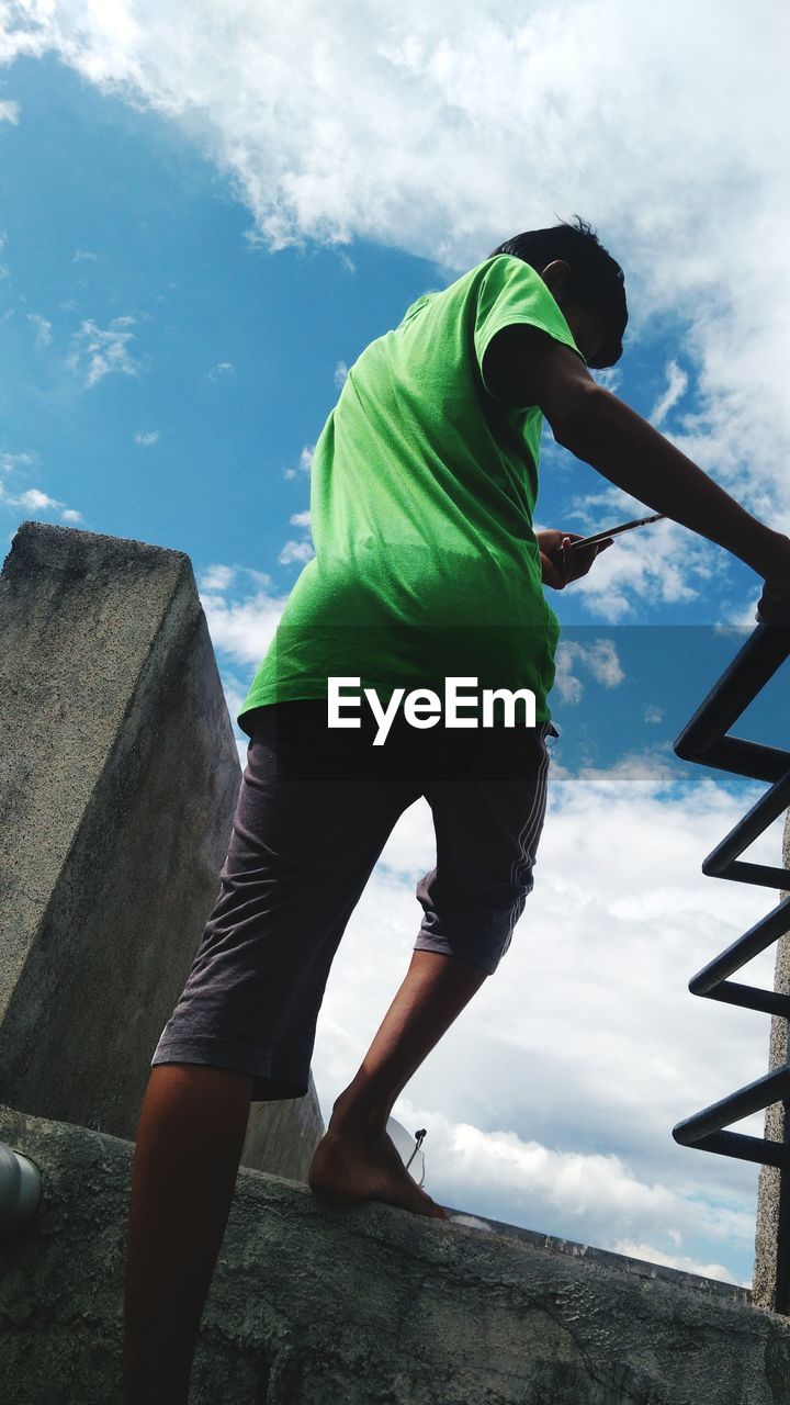 LOW ANGLE VIEW OF MAN STANDING ON MOUNTAIN AGAINST SKY