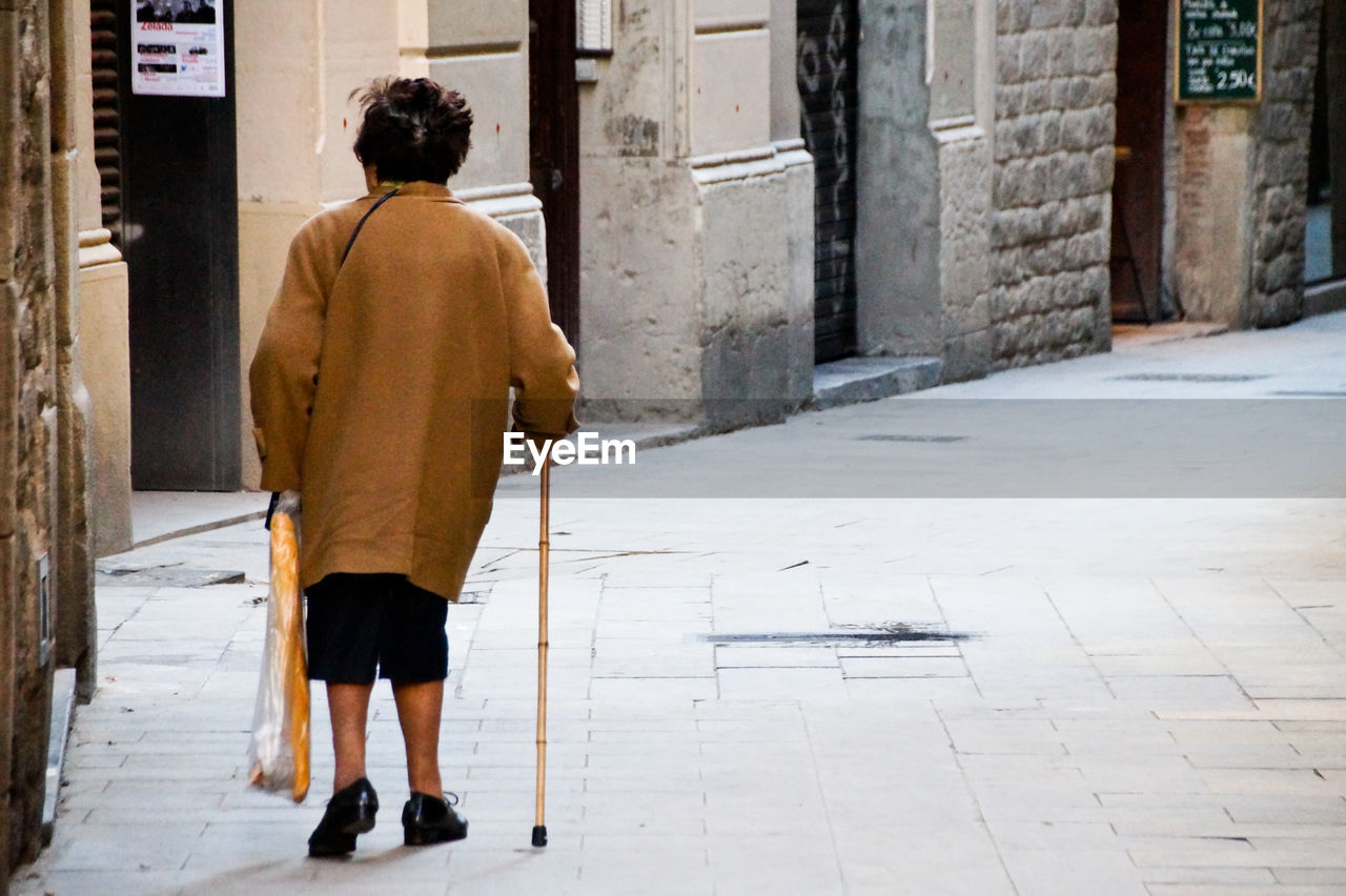Rear view of pensioner walking on street in city