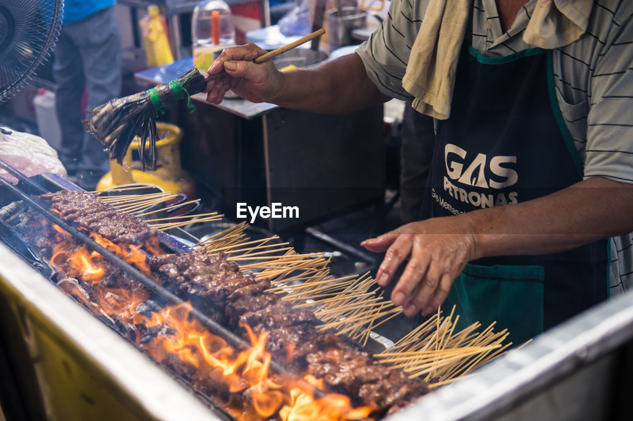 MIDSECTION OF MAN PREPARING FOOD ON BARBECUE GRILL AT MARKET