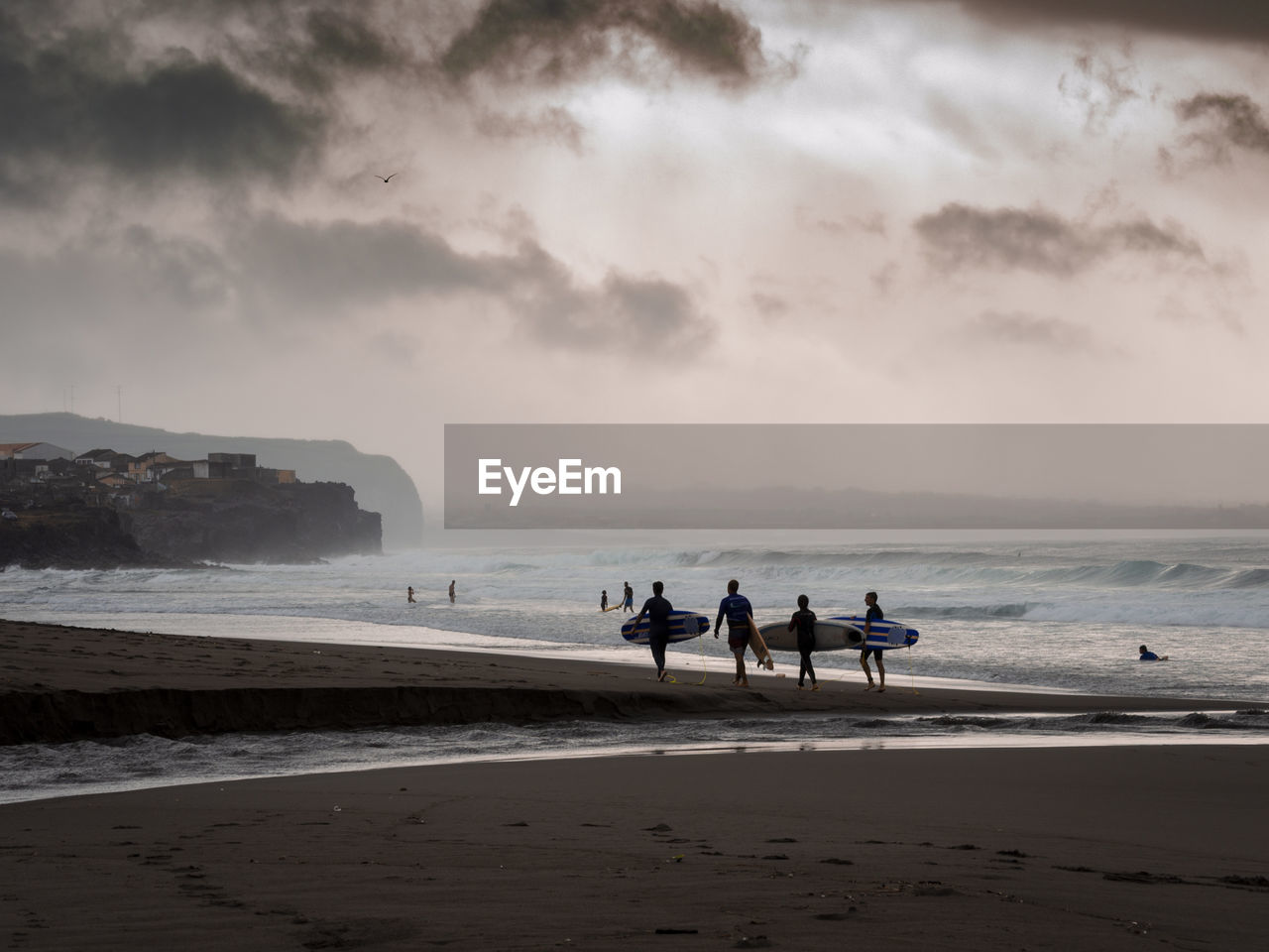 Full length of friends with surfboards walking at beach against sky during sunset