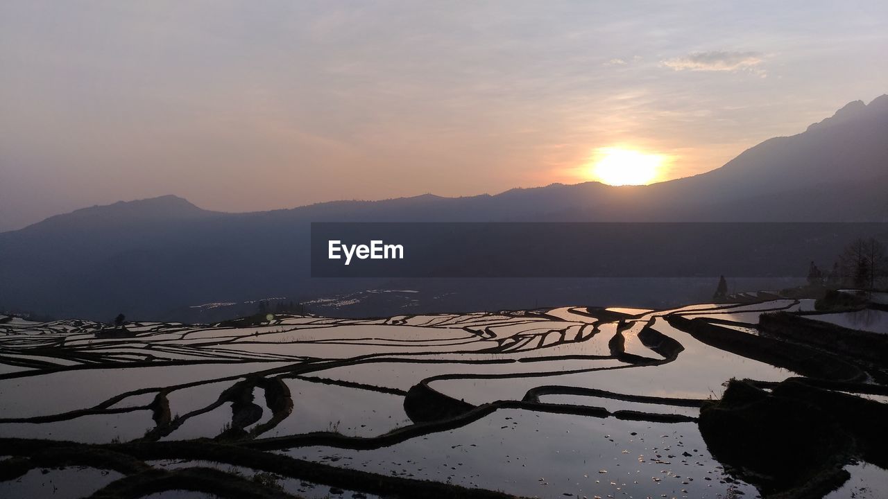 SCENIC VIEW OF LAKE BY SILHOUETTE MOUNTAINS AGAINST SKY DURING SUNSET