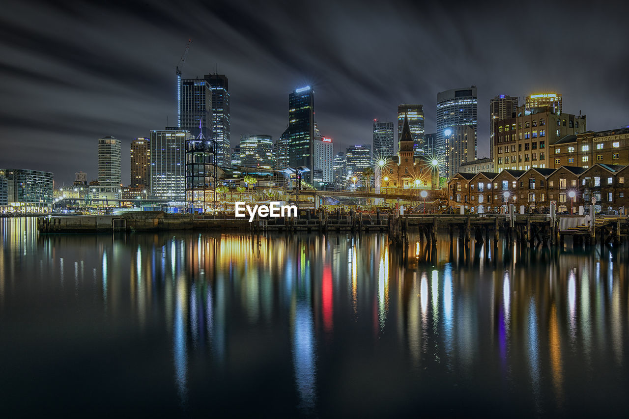 ILLUMINATED BUILDINGS BY RIVER AGAINST SKY