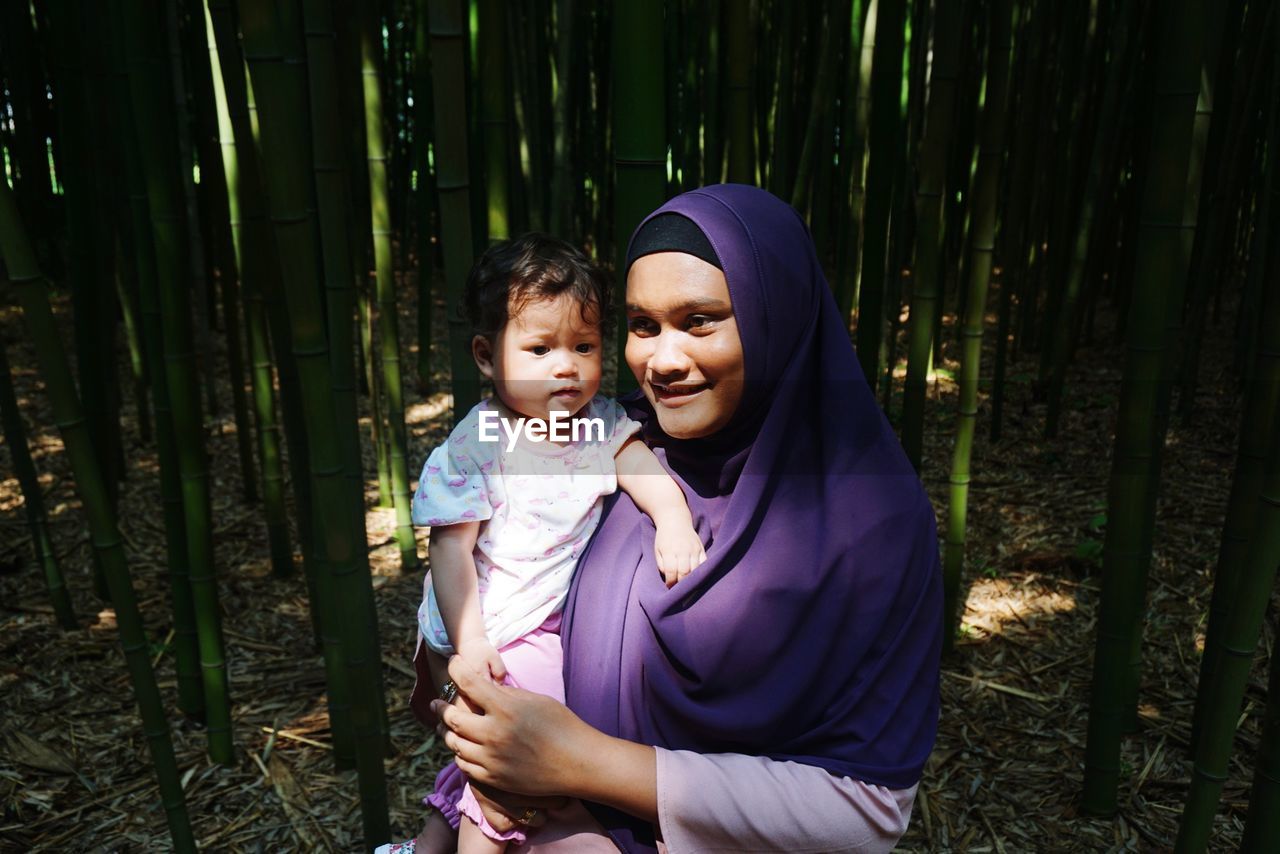 Woman carrying daughter while standing at bamboo grove