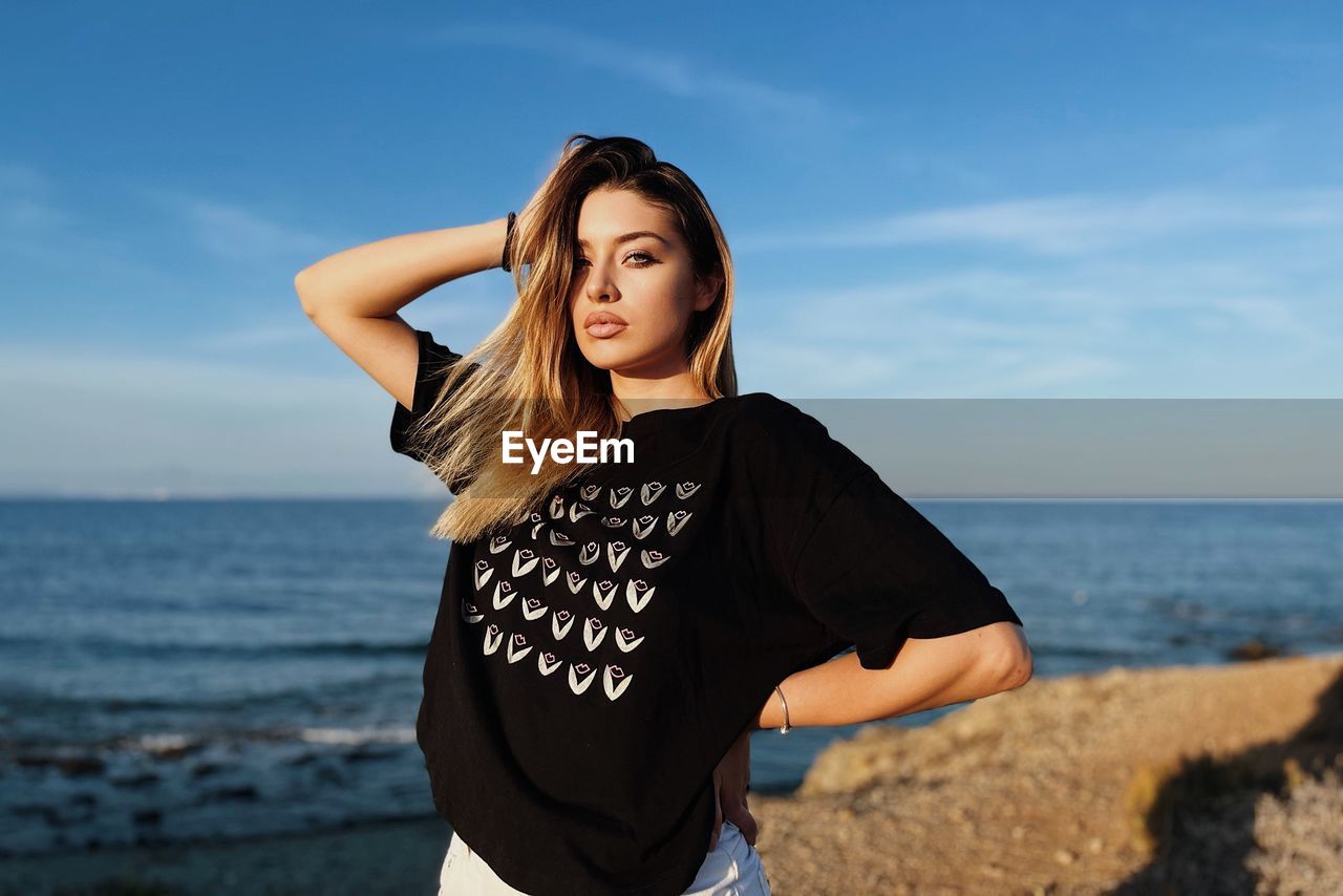 Young woman standing at beach against sky during sunset