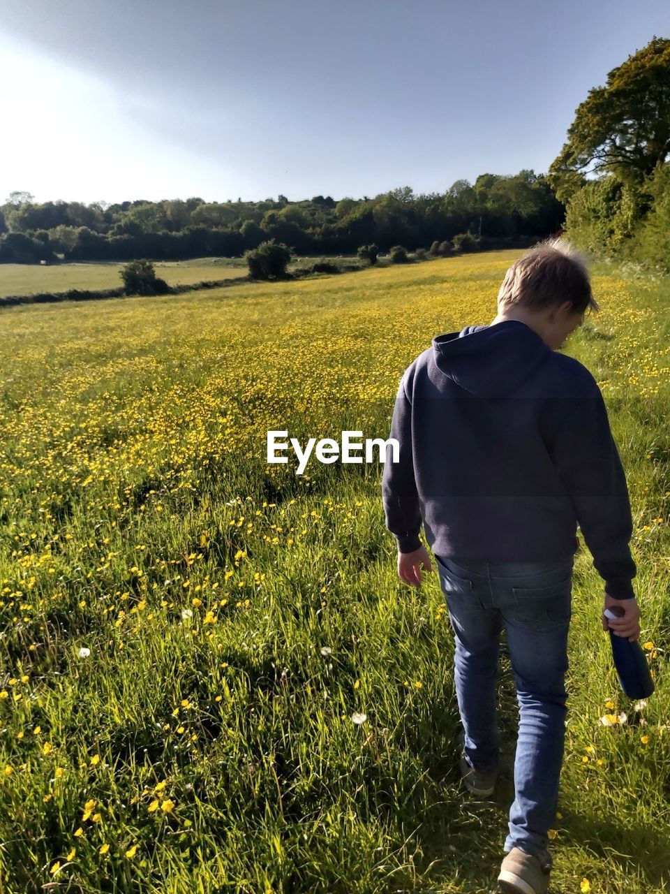 REAR VIEW OF MAN STANDING ON FIELD AGAINST SKY