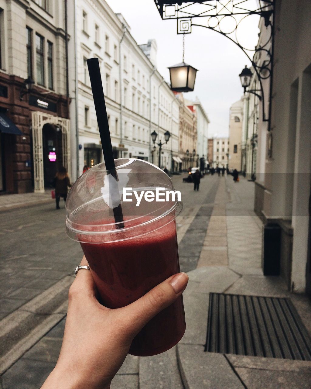 CLOSE-UP OF HAND HOLDING DRINK AGAINST BUILDING