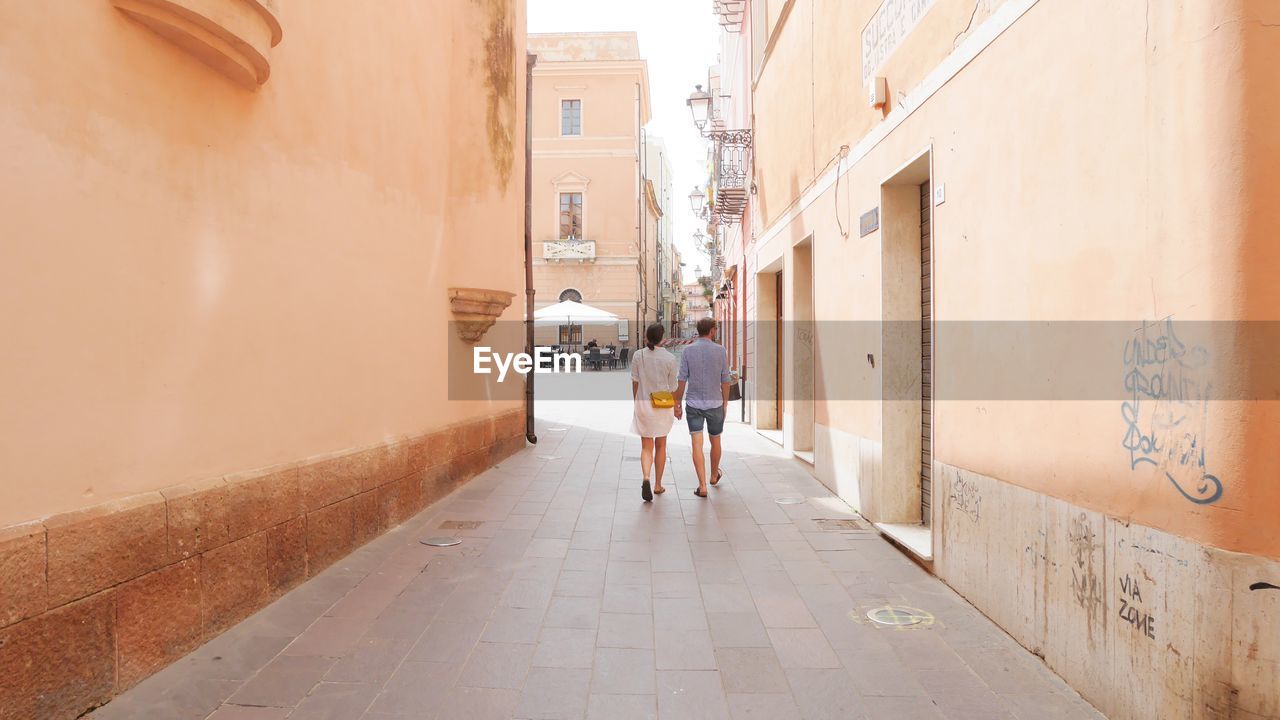 Rear view of couple walking on footpath amidst buildings in city