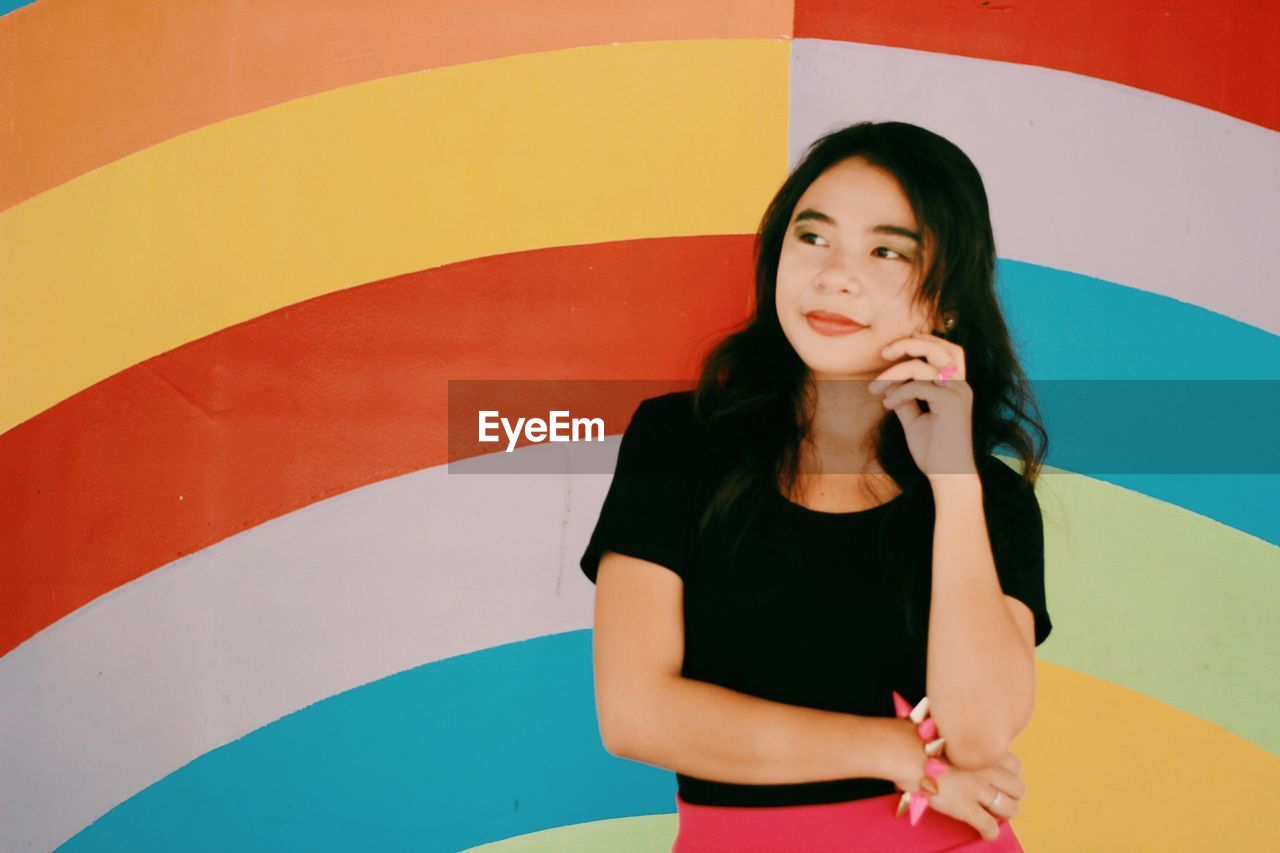 YOUNG WOMAN STANDING AGAINST WALL